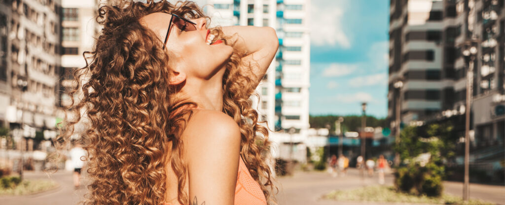 5 Essential Secrets to Defined, Frizz-Free Curls portrait of beautiful smiling model with afro curls hairstyle dressed in summer hipster clothes.sexy carefree girl posing in the street background. trendy funny and positive woman having fun